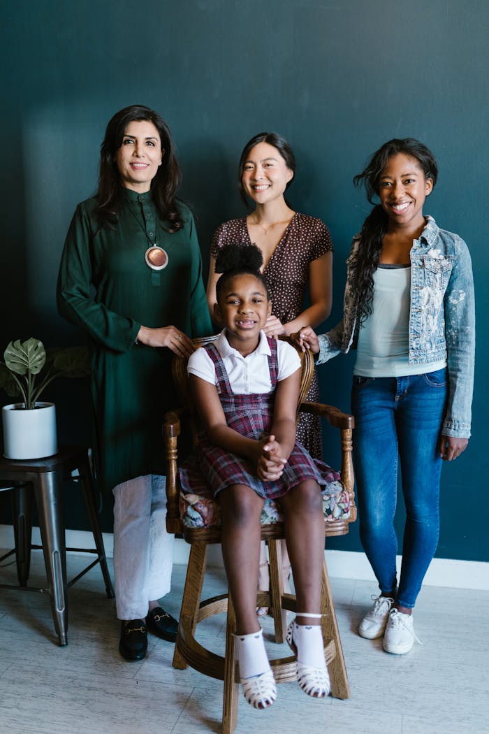A diverse group of women and a girl smiling indoors, showcasing inclusivity.