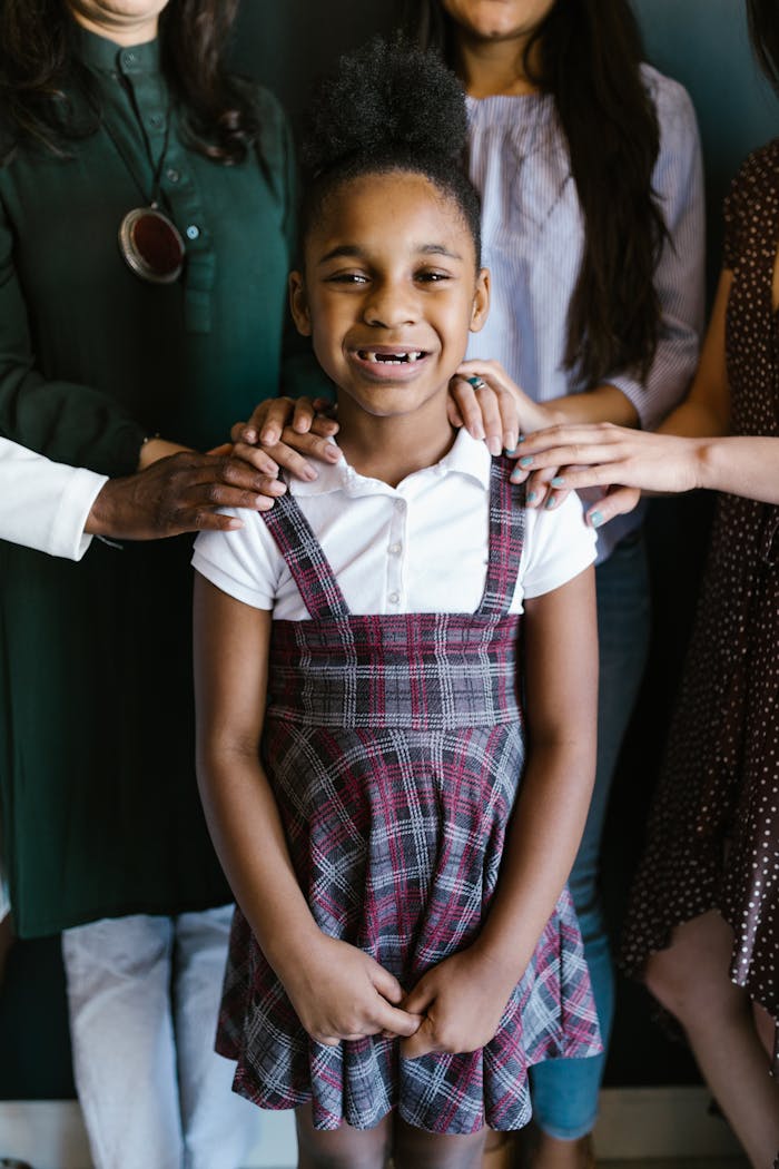 A smiling young girl surrounded by adults hands in a show of united support and empowerment.